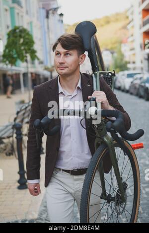 Hübscher reifer Mann, der sein Fahrrad auf der Schulter trägt und durch die Straßen der Stadt geht Stockfoto