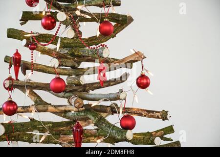 Hausgemachter rustikaler Weihnachtsbaum aus rohem Holz Ästen, dekoriert mit Lichterketten und roten Kugeln, nachhaltiger und umweltfreundlicher Alternat Stockfoto