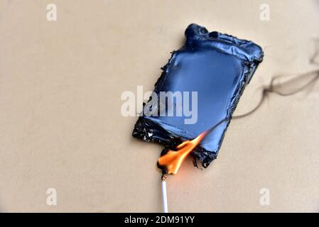 Mobiltelefon hat Feuer aus dem Kabel mit dem Aufladen aus dem elektrischen Netz in der Steckdose gefangen. Kostengünstige Ladegeräte gefährden Ihre Zelle. Kabel o Stockfoto