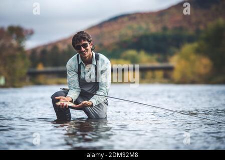 Der Mensch hält Regenbogenforelle im Fluss mit Laub im Hintergrund Stockfoto