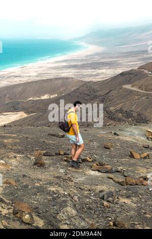 Landschaft mit einem Mann, der zwischen Meer und Bergen wandert. Reisen durch den Jandia Park auf Fuerteventura. Stockfoto