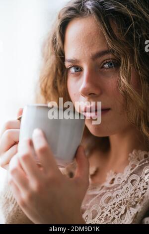 Junge Frau mit blauen Augen nippend heißen Drink und suchen Bei der Kamera Stockfoto