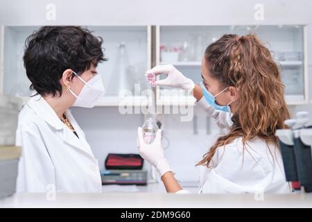 Zwei junge Wissenschaftlerinnen tragen Gesichtsmasken mit einer Flasche. Laborforschungskonzept. Stockfoto