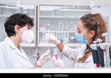 Zwei junge Wissenschaftlerinnen mit Gesichtsmasken während eines Experiments in einem Labor. Laborforschungskonzept. Stockfoto