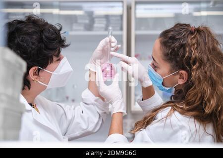 Zwei junge Wissenschaftlerinnen tragen Gesichtsmasken mit einer Flasche. Laborforschungskonzept. Stockfoto