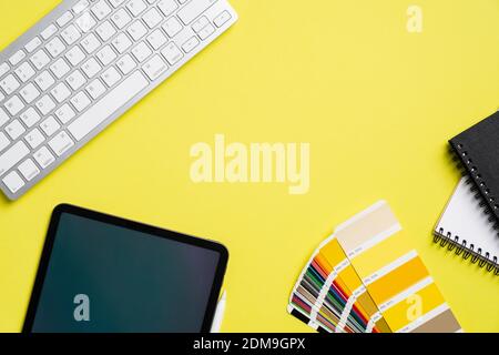 Grafikdesigner Büro-Desktop mit Tablet, Farbführer-Palette, Tastatur, Papier Notizbücher auf gelbem Hintergrund. Kreativer professioneller Arbeitsplatz, Vie Stockfoto