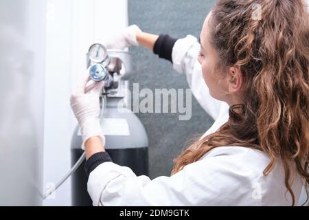 Junge Wissenschaftlerin beim Öffnen einer Gasflasche mit Manometer in einem spezialisierten Labor. Laborforschungskonzept. Stockfoto