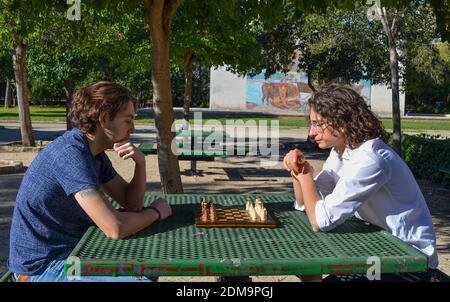 Eine Nahaufnahme von zwei Jungs spielen Schach in der park in der Nähe der Bäume auf der Bank Stockfoto