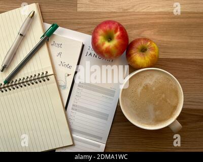 Kalender auf dem Schreibtisch, mit Notizbüchern, Stiften, Kaffee und Äpfeln Stockfoto