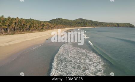 Die Wellen fallen in die Antenne des Sandmeeres. Wellige Meereslandschaft der Ocean Bay. Sandige Küste mit tropischem Wald. Hügel mit grünen Dschungel von Palmen. Paradiesischer Urlaub auf El Nido Island, Philippine, Asien im Sommer Stockfoto