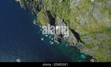 Passagierboote an der Klippe Ozeanküste bei ruhiger Seeufer Luftaufnahme. Majestätische Natur auf Felseninsel mit tropischen Pflanzen. Sommerurlaub Landschaft der Kreuzfahrt-Tour auf traditionellen Schiffen der Philippinen. Stockfoto