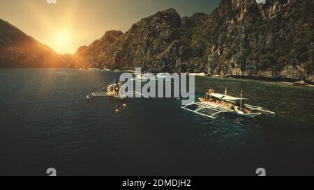 Seascape mit Passagierbooten bei Sonnenuntergang in Nahaufnahme Luftaufnahme. Cliff Coast mit grünen Bäumen an sonnigen Sommertagen. Philippinen Urlaub mit Touristen schwimmen am Meer Wasser. Sun set filmische Drohne aufgenommen Stockfoto