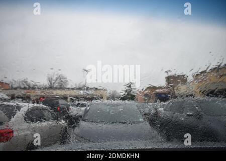 Ich habe in einem Einkaufszentrum im Regen geparkt und dabei auf die Straße geschaut Durch eine nasse Windschutzscheibe -03 Stockfoto