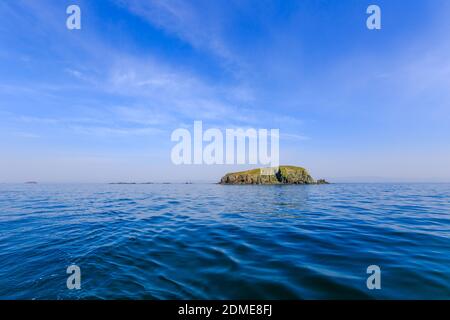 Eine kleine unbewohnte grüne Insel inmitten eines ruhigen blauen Meeres und blauen Himmels. Schöne Entspannung Hintergrund Stockfoto