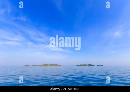 Eine kleine unbewohnte grüne Insel inmitten eines ruhigen blauen Meeres und blauen Himmels. Schöne Entspannung Hintergrund Stockfoto