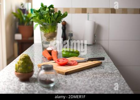 Paprika auf einem Schneidebrett und frische Zutaten über einer Küchenarbeitsplatte. Stockfoto