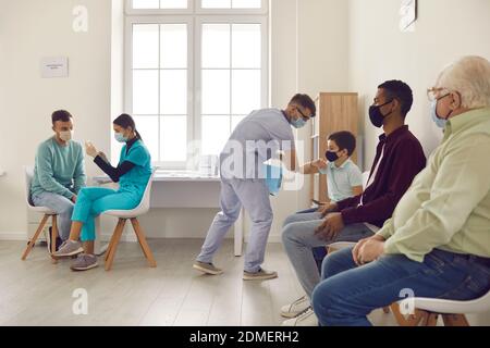 Verschiedene Menschen in medizinischen Gesichtsmasken sitzen in der Schlange, warten auf Grippe oder Covid-19-Impfstoff zu bekommen Stockfoto