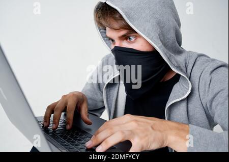Ein Mann in einer Maske sitzt auf dem Boden innen Vor einem Laptop-Computer Hacking Verbrechen Stockfoto