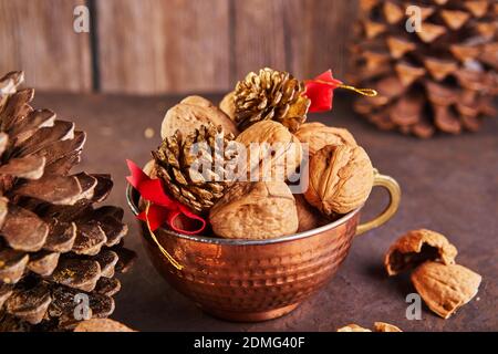 Walnüsse in einem Blechbecher, ganz und gehackt, neben der Füllung und Schalen. Präsentiert in einer Neujahrskomposition mit Tannenzapfen. Home Lagerung des Winters Stockfoto