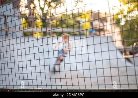 Ein Spielplatz mit Rutschen hinter einem Gitterzaun. Jungen fahren Skateboards und Roller, verschwommener Hintergrund. Gefährlicher Sport. Stockfoto