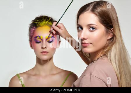 Weibliche Porträt mit ungewöhnlichen Gesicht Kunst Make-up. Farbe auf Augenbrauen, Haare und um die Augen. Künstler Hand mit Pinsel Malerei schöne Mädchen Brauen machen Stockfoto