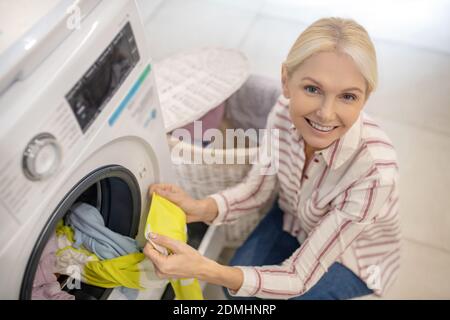 Blonde Frau, die Kleidung in die Waschmaschine legt Stockfoto