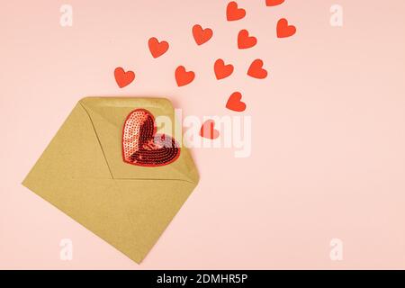 Papierhandwerk Umschlag mit streuenden roten Herzen auf rosa Hintergrund. Mit Kopierbereich. Kreatives Layout für den Valentinstag Stockfoto