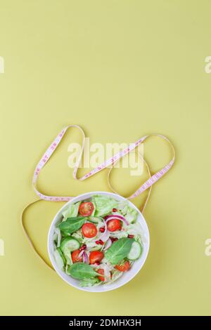 Gesunde ausgewogene Ernährung Konzept, Salat mit Gurken Tomate Zwiebel Salatblätter mit Maßband auf gelbem Hintergrund. Draufsicht copy space Stockfoto