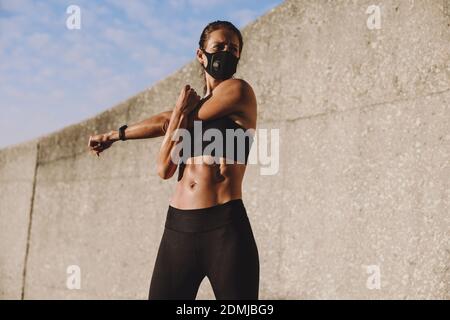 Sportliche Frau mit schützender Gesichtsmaske, die die Hände vor dem Training dehnt. Frau macht Warmup Training im Freien. Stockfoto