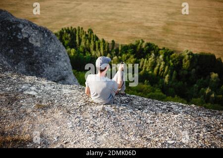 Rückansicht eines jungen Mannes, der Tee oder Kaffee in den Bergen trinkt. Reisender Mann mit Bart hält in den Händen eine Tasse Tee, nach dem Wandern. Reisen, Lifestyle, VA Stockfoto