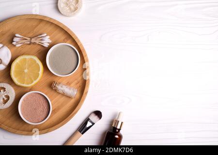 Kosmetische Ton Gesichtsmasken, Meersalz, Zitrone und Pinsel auf weißem Holzhintergrund. Flache Lay-Optik. Stockfoto