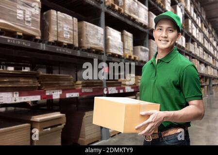 Asiatische Lieferung Mann oder Passagier hält einen Karton mit Logistiklager im Hintergrund Stockfoto