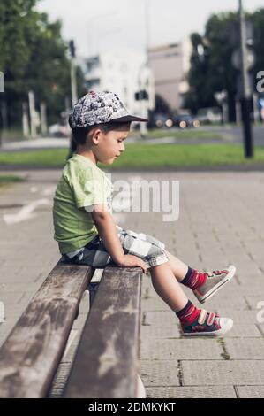 POZN, POLEN - 18. Aug 2017: Kleiner Junge sitzt auf einer Holzbank an einer Straße in der Stadt Stockfoto