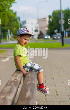 POZN, POLEN - 18. Aug 2017: Kleiner Junge sitzt auf einer Holzbank an einer Straße in der Stadt Stockfoto