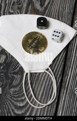 Bitcoin liegt auf einer medizinischen Maske. Würfel sind in der Nähe verstreut. Auf Kiefernbrettern. Stockfoto