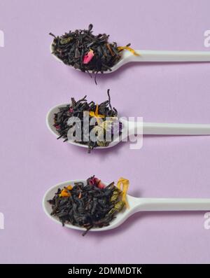 Plastiklöffel mit trockenen Teeblättern auf violettem Hintergrund. Stockfoto