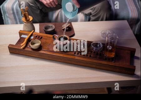 Nahaufnahme mit einem verschwommenen Hintergrund, gießen Hände heißen duftenden köstlichen Tee aus einem Tablett Teekanne in spezielle zeremonielle Tassen Stockfoto