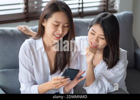 Two asian woman enjoy watching photo on mobile phone at home Stockfoto