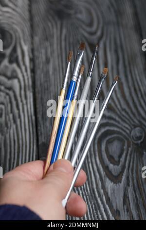 Ein Mann hält Pinsel in der Hand. Vor dem Hintergrund von schwarzen Kieferntafeln. Stockfoto