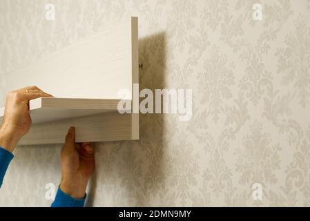 Der Hausmeister hängt das Regal an Betonwand mit Tapeten. Meister montiert Möbel. Stockfoto