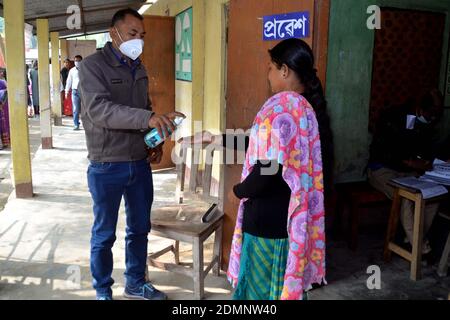 Nagaon, Assam, Indien - 17. Dezember 2020: Ein Gesundheitsarbeiter sprüht Handdesinfektionsmittel an alle Wähler, die wegen einer Pandemie von Covid - 19 in einer Polling-Station während der Tiwa Autonomen Ratwahl im Dorf Kachamari im Bezirk Nagaon in Assam, Indien, in der Schlange stehen. Kredit: DIGANTA TALUKDAR/Alamy Live Nachrichten Stockfoto