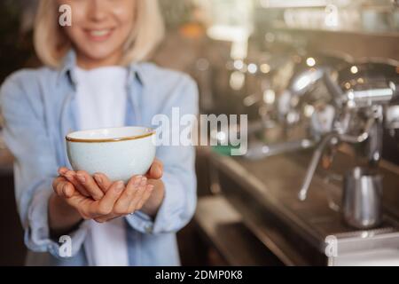 Zugeschnittene Aufnahme einer Barista, die eine Kaffeetasse an die Kamera hält, Platz kopieren. Nicht erkennbare Frau, die dem Betrachter eine Tasse Kaffee anbietet Stockfoto