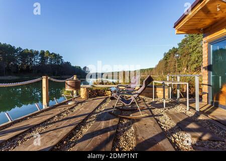 Schaukelstuhl auf einem hölzernen Pier am See. Haus auf dem Wasser. Ruhestätte vor dem Hintergrund einer herbstlichen Landschaft Stockfoto