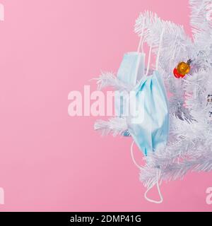 closeup of some blue disposable face masks hanging from the branches of a white christmas tree, against a pink background Stock Photo