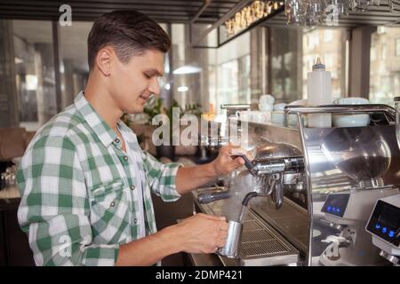 Attraktiver junger Barista, der im Café arbeitet und einen Drink auf der Kaffeemaschine zubereitet. Service, Café, Stadtleben Konzept Stockfoto