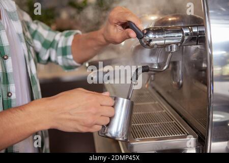 Cropped shot of unrecognizable male barista steaming milk for delicious cappuccino. Professional barista preparing coffee for a customer, using coffee Stockfoto