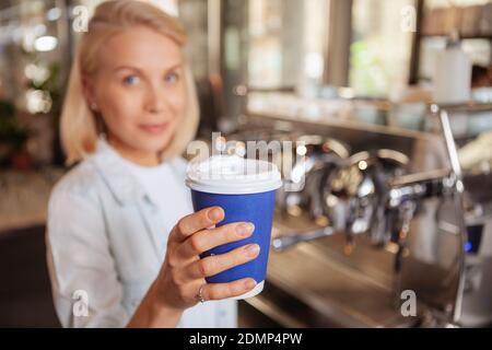 Konzentriere dich selektiv auf eine recycelbare Kaffeetasse aus Papier, die von einer Barista aus der Hand kommt. Schöne Frau bietet Tasse Kaffee zu gehen, um den Betrachter Stockfoto