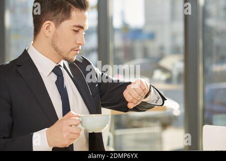 Timing ist alles. Hübscher junger Geschäftsmann, der die Zeit auf seiner Uhr mit einer Tasse Kaffee überprüft Stockfoto