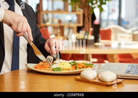 Mittagspause. Nahaufnahme eines Geschäftsmannes, der während des Geschäftsessen im Restaurant Essen auf seinen Teller schneidet Stockfoto