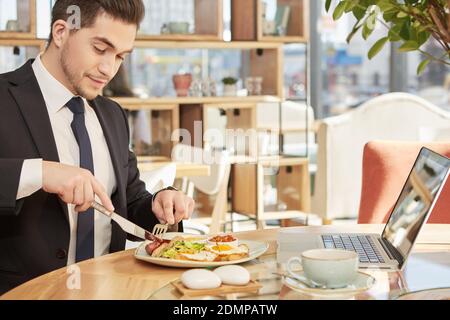 Sag nein zum Hunger. Horizontale Aufnahme eines gutaussehenden, fröhlichen Geschäftsmannes, der sein Mittagessen im lokalen Restaurant genießt Stockfoto